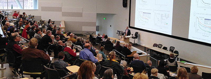 A group of attendees watching a presentation at a melanoma conference.