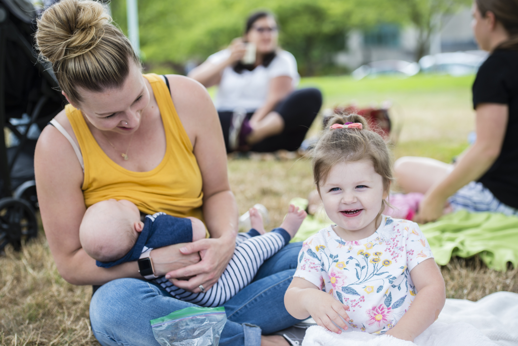 Woman nurses young baby while toddler smiles at camera