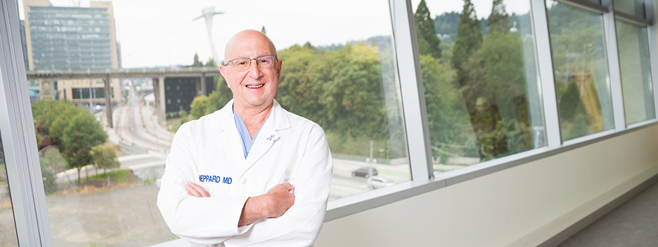 OHSU surgeon Brett Shepard smiles as he stands by a window with a view of OHSU’s main campus.