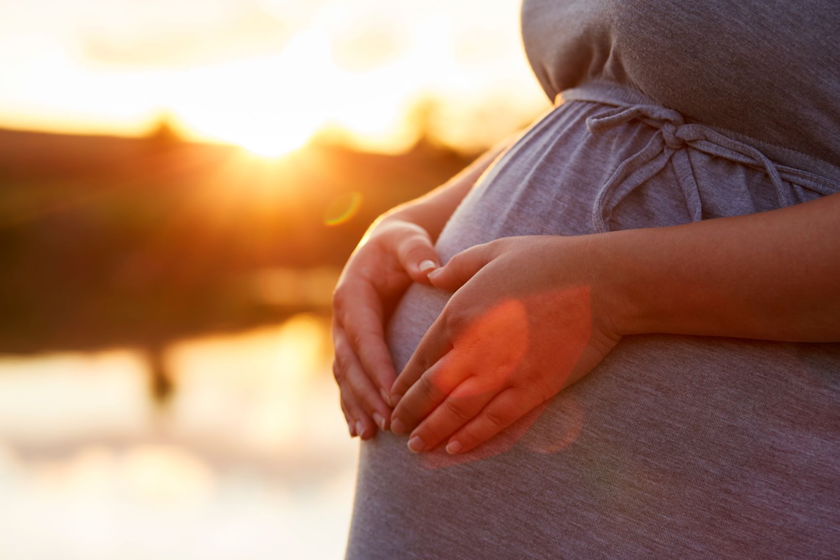 Pregnant woman makes heart with her hands on her belly.