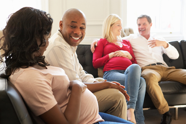 Two pregnant couples shown sitting together.