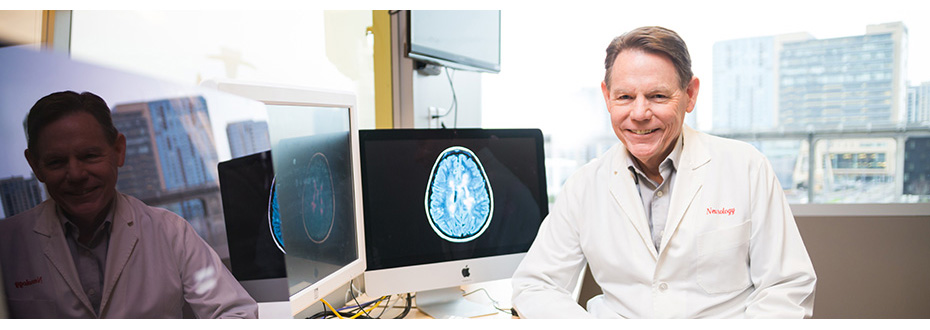 Dr. Dennis Bourdette, M.D., FANA, FAAN, in a lab coat in front of a computer at the OHSU Multiple Sclerosis Center