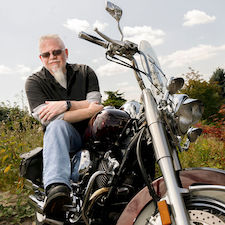 A healthy patient takes a break from riding a motorcycle along a country road.