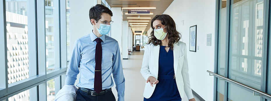 Two doctors, a man and a woman, talk while walking down a hallway at OHSU