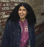 A woman smiling in front of a brick wall at night.