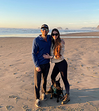 A woman poses with a man and their dog on the beach.