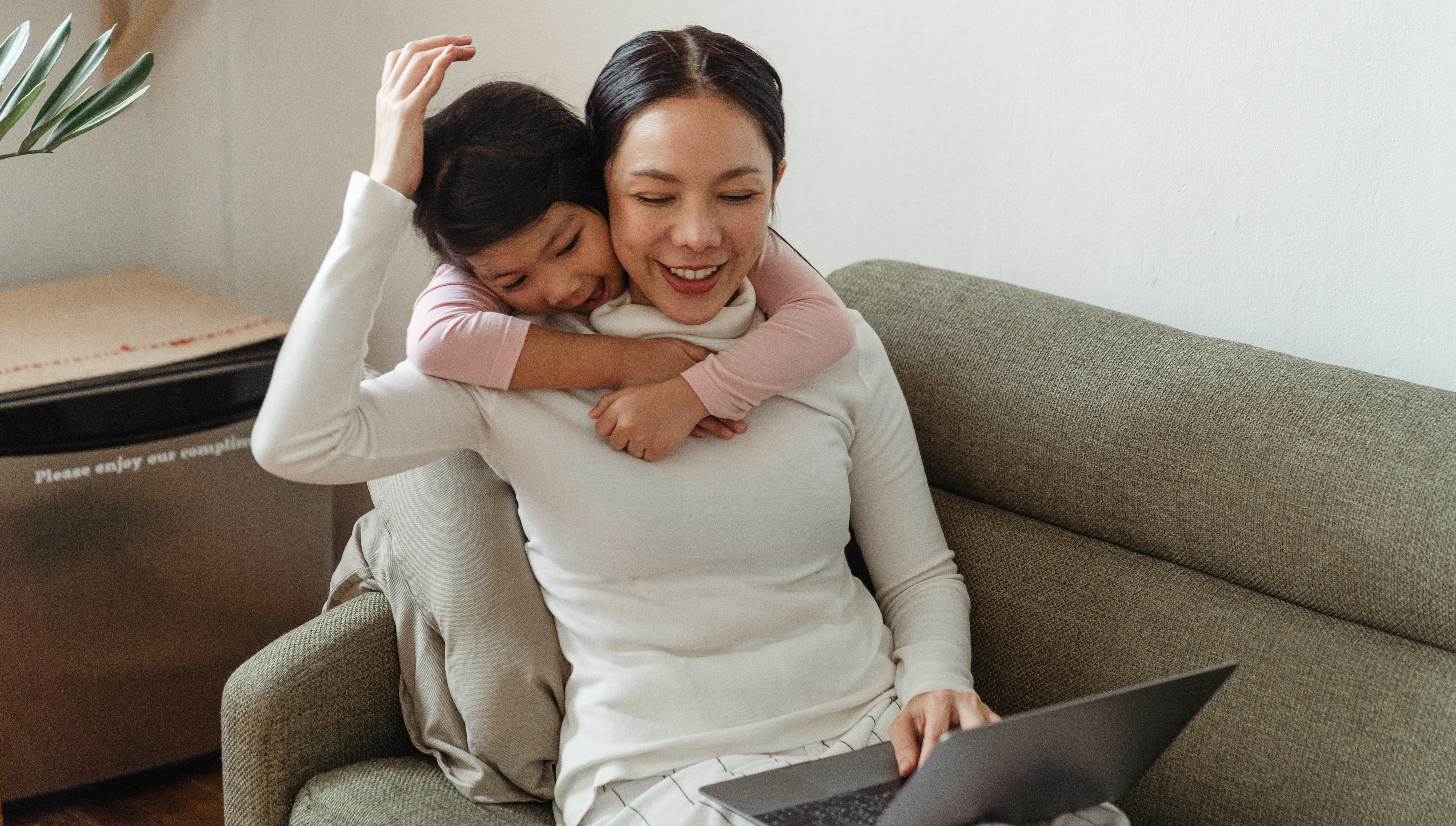 A parent participates in a group video call as their cheerful daughter hugs them from behind.