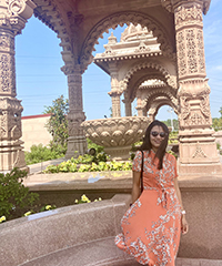 A woman smiling outside beneath an architectural structure.