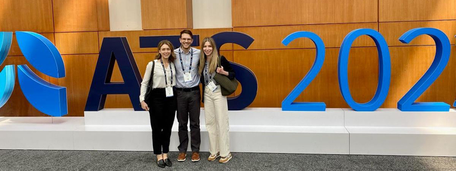 A man stands in between two women in front of giant letters that read "ATS 2023."