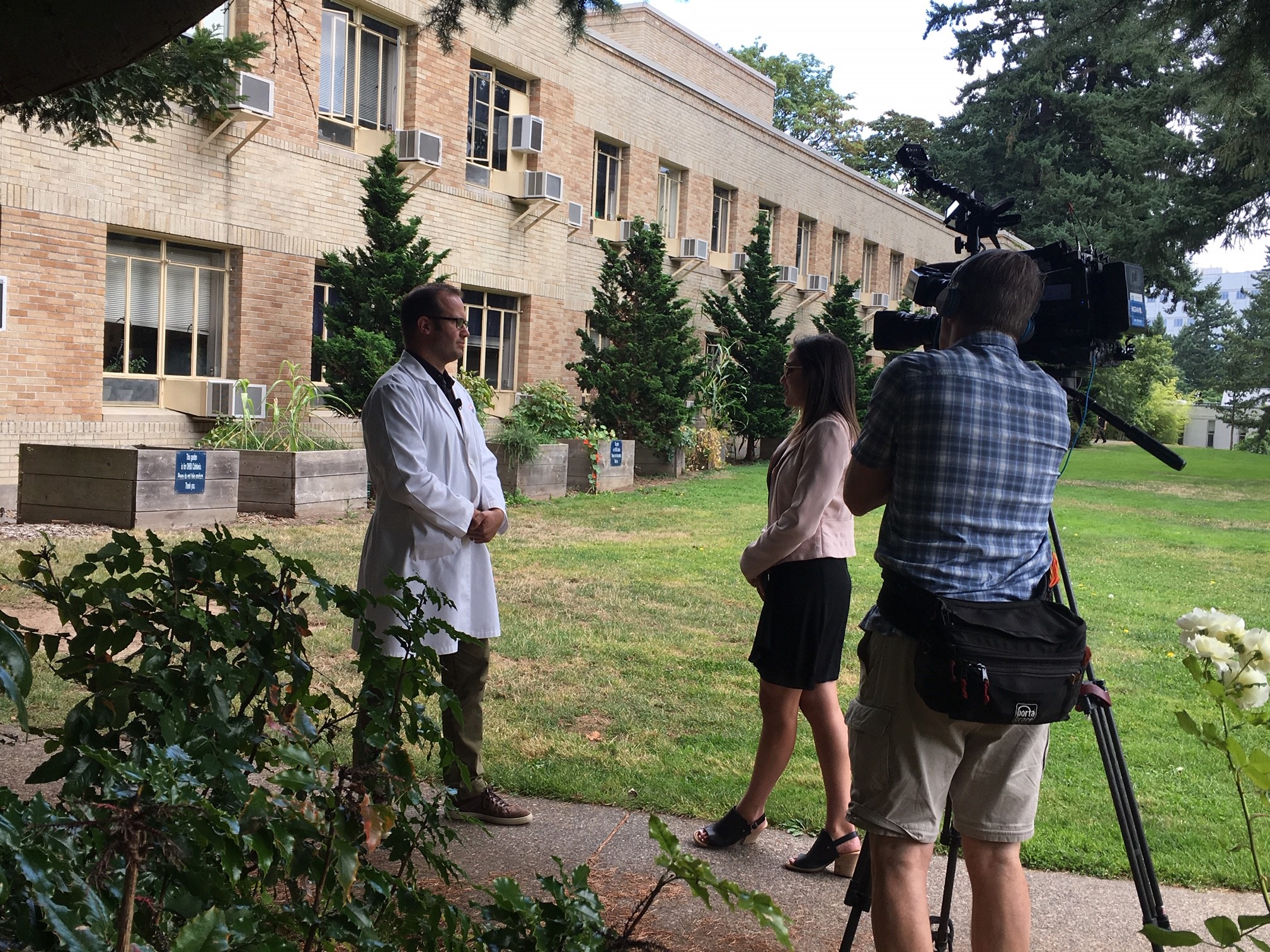 Dr. Rob Hendrickson provides a television interview on the lawn behind the Central Services Building at OHSU