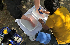 A street nursing team OHSU student washes a pair of feet in white basins resting on the ground.
