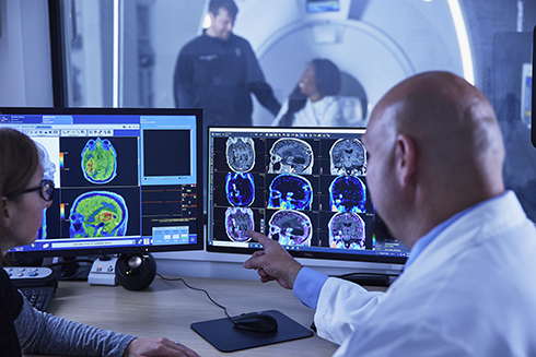 Two OHSU employees discuss PET and MRI scan images on two monitors.