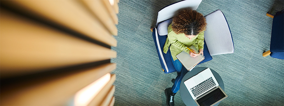 Overhead view of a nursing student sitting in a blue chair, working with a laptop and notebook.