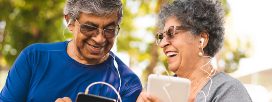 Two older adults looking at tech devices outside smiling