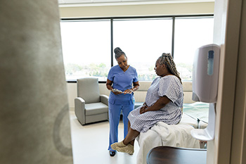 An OHSU nursing student wearing scrubs reviews information on a tablet with a patient in a clinical setting.
