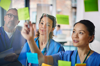 Three OHSU nursing students wearing scrubs review patient information.