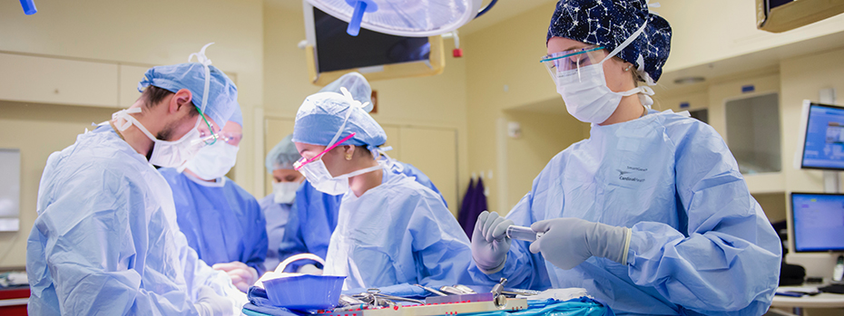 A group of health care providers are dressed in blue scrubs and prepping for a surgery in an operating room.