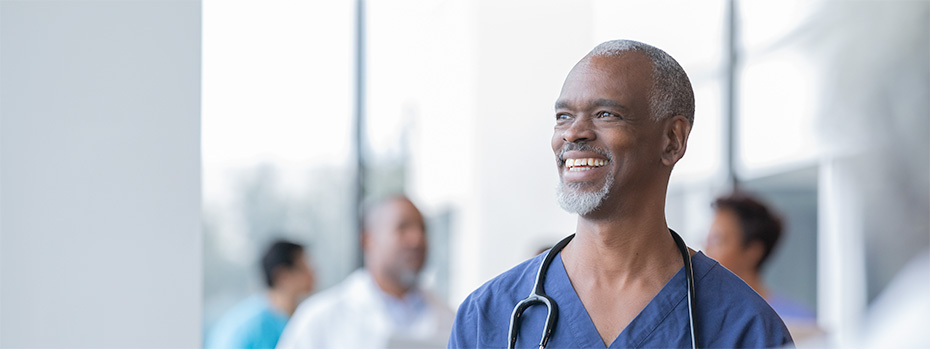 A student wearing blue scrubs and a stethoscope smiles and looks off into the distance.