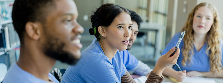 Four nursing students in scrubs sit at a table