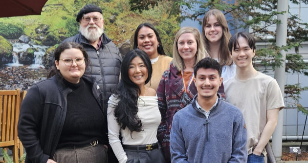 Nine members of the OHSU BRAIN Lab pose together in front of the Portland VA, building 1.