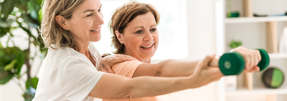 An exercise physiologist teaches a woman how to lift a dumbbell.