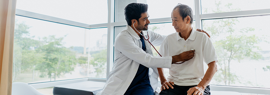 A doctor uses a stethoscope to listen to the heartbeat of a male patient in a doctor’s office.