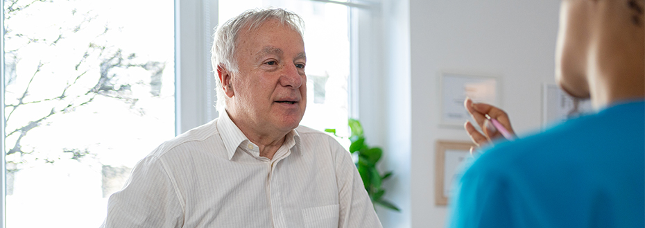 A male patient speaks with a male doctor in an exam room.
