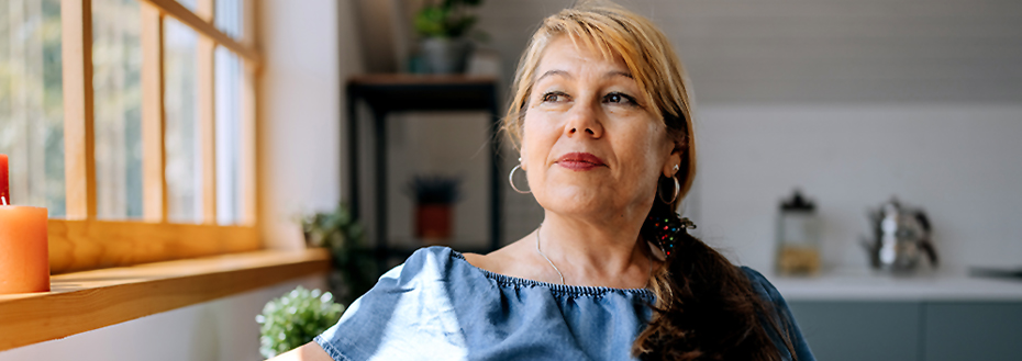 Woman in her sixties sits in front of a window in her home.