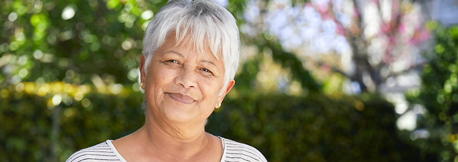 Portrait of a woman in her sixties outside in front a hedge.