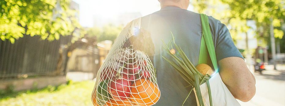 A person walks down the street while carrying bags of groceries with fresh produce and vegetables in them.
