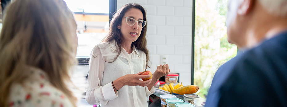 A registered dietitian speaks with patients while holding an apple in a bright kitchen.