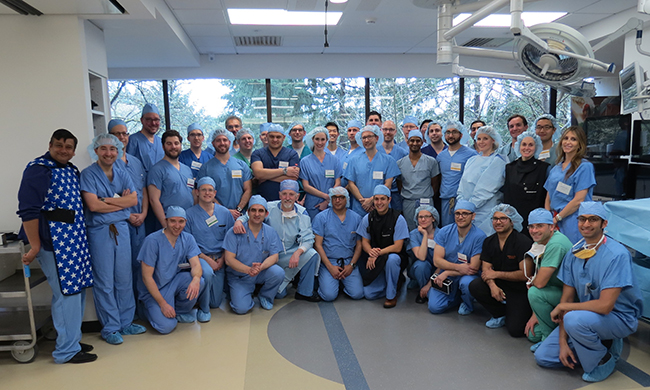 A group of 40 doctors, trainers, residents and fellows in a lab all wearing hospital scrubs.