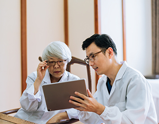 Two health care providers look at a digital tablet together.