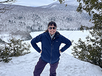 A woman standing with her hands on her hips smiling on a snowy day.