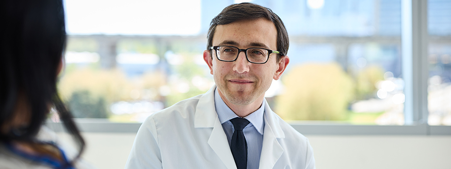 A doctor smiles while listening to a patient in a hospital room.