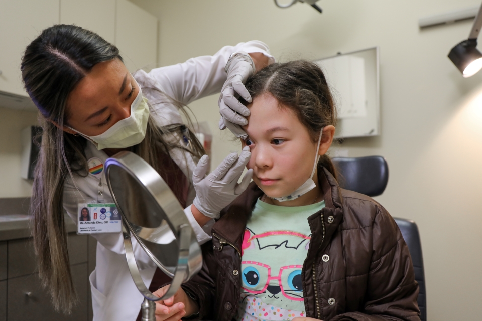Dr. Amanda Dieu helps a preteen girl put in her contact lens.