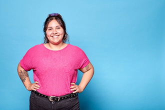 A woman in a bright pink shirt stands smiling with her arms on her hips.