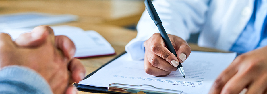 A person holds a pen and writes on paper attached to a clipboard.