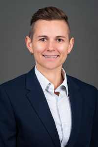 A professional head shot of Dr. Monica Llado-Farrulla in a light blue collared shirt and a navy blazer.
