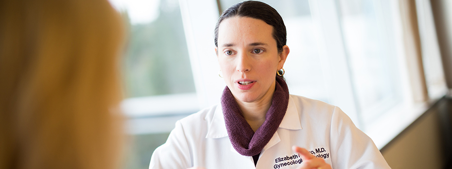 A female doctor stands in front of a window speaking to a patient.