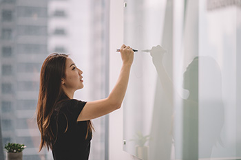 A woman writes on a whiteboard during a planning or brainstorming session.