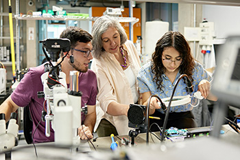 A faculty member works with two students in a lab setting.
